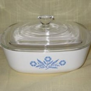 May include: A white square baking dish with a blue floral design and a clear glass lid. The dish has two handles on the sides.