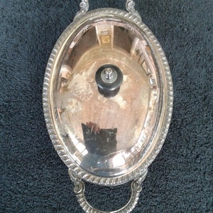 May include: Silver oval serving dish with a lid and two handles. The dish has a decorative border and a knob on the lid.