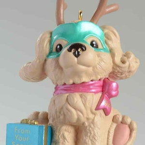 May include: A light brown dog wearing a green mask and reindeer antlers, holding a blue box with the text "From Your Secret Pal".
