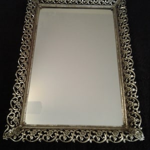 May include: A silver-toned decorative tray with a mirrored surface and an ornate, floral design around the border.