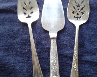 May include: Three silver cake servers with ornate handles. The servers have a decorative cut-out design on the front.