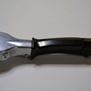 May include: A black and silver pot handle with a metal loop. The handle is black and has a geometric shape. The silver part is attached to the black handle and has a unique shape.