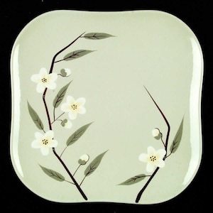 May include: A square, light green ceramic plate with a floral design. The design features white flowers and green leaves on brown branches.