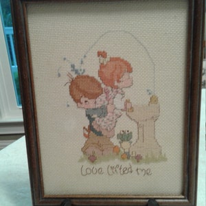 May include: A framed cross-stitch with a picture of two children standing at a fountain. The text "Love lifted me" is below the image.