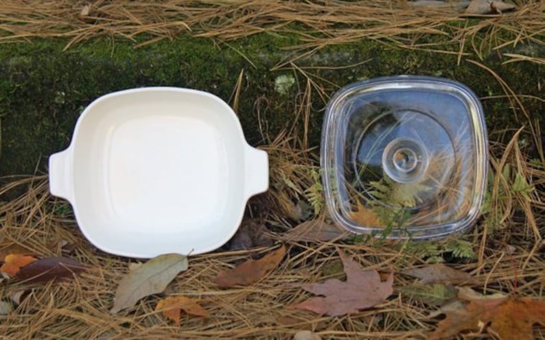 May include: A white ceramic baking dish with a glass lid. The dish is square and has rounded corners. The lid is clear and has a slightly raised rim.
