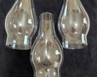 May include: Three clear glass lamp chimneys with a bulbous midsection and a straight, cylindrical top opening. These transparent glass shades feature a smooth, curved silhouette designed to fit over a light source or candle flame.