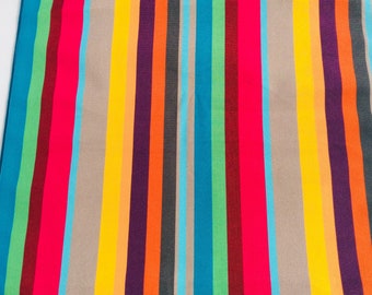 Op de afbeelding: Een kleurrijke gestreepte stof met afwisselende banden in beige, geel, oranje, paars, rood, teal, groen en donkerrood.