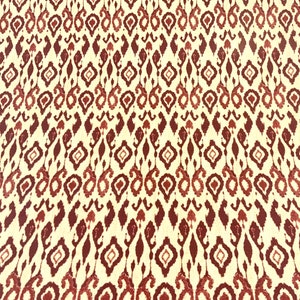 Może przedstawiać: Biała tkanina z powtarzającym się wzorem czerwonych i brązowych kształtów geometrycznych. Wzór jest tradycyjnym wzorem ikat.