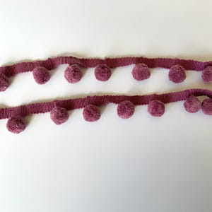 May include: A length of mauve trim with a row of fluffy pom-poms along each edge.