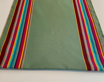 Op de afbeelding: Een groene tafelrunner met kleurrijke strepen. De strepen zijn rood, roze, geel, blauw en turquoise.