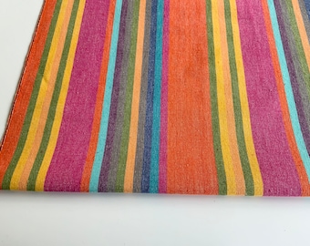 Puede incluir: Una tela de rayas coloridas con una variedad de colores, incluyendo naranja, amarillo, verde, azul y rosa. La tela está doblada en la parte inferior.