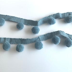 May include: A light blue trim with pom poms. The trim is made of a soft, fuzzy material and has a subtle sheen.