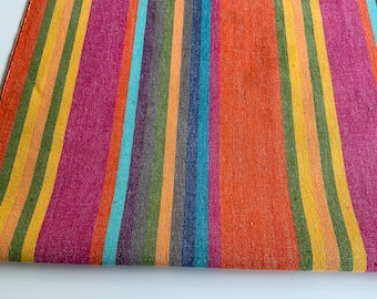 Op de afbeelding: Gestroomde stof met afwisselende banden in oranje, geel, groen, blauw, paars en roze.
