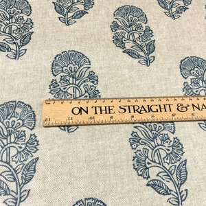 May include: A close-up of a beige fabric with a repeating pattern of dark blue floral designs. A wooden ruler with the text "ON THE STRAIGHT & NARROW" is placed on top of the fabric.