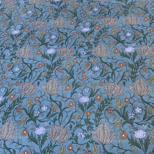 Peut inclure: Un tissu à motifs floraux. Le motif présente de grandes fleurs beiges, de petites fleurs orange et blanches, ainsi que des feuilles et des vignes vertes sur un fond bleu clair. L'ensemble évoque des imprimés botaniques vintage, idéal pour les projets créatifs.