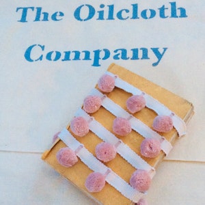 May include: A small, yellow book with a white and pink trim. The book has the text "The Oilcloth Company" printed on the cover.