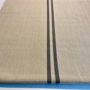 May include: A rectangular beige linen table runner with two vertical charcoal gray stripes running down the center. The fabric has a textured appearance, and the runner is displayed on a white surface.
