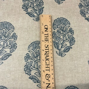 May include: A close-up of a beige fabric with a repeating pattern of dark blue floral designs. A wooden ruler with the text "ON THE STRAIGHT & N" is visible on the right side of the image.