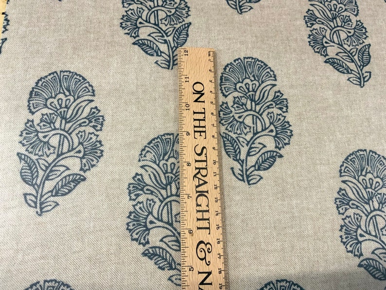 May include: A close-up of a beige fabric with a repeating pattern of dark blue floral designs. A wooden ruler with the text "ON THE STRAIGHT & N" is visible on the right side of the image.