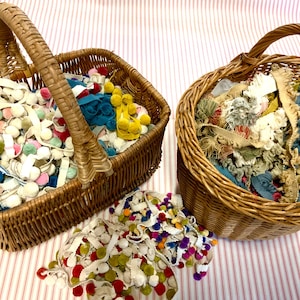 May include: Two wicker baskets filled with colorful fabric scraps and pom poms. The baskets are on a pink and white striped surface.
