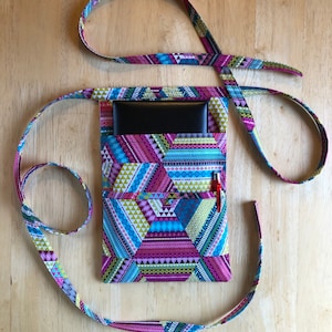 May include: A colorful geometric patterned fabric pouch with a black pocket and a red pen inside. The pouch has a long pink and blue strap.