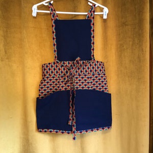 May include: A navy blue apron with rainbow-colored trim and a rainbow pattern. The apron has two large pockets on the front.