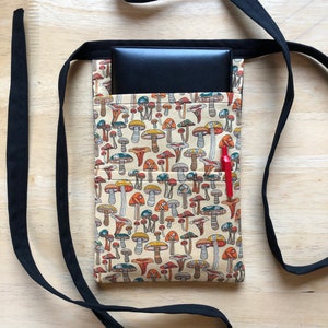 May include: A black fabric belt with a beige pouch featuring a mushroom print. The pouch has a black zipper and a red pen sticking out of the top.