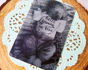 May include: A black and white photo of a baby wearing a grey onesie with the text "hello world I'm Luca" printed on it.