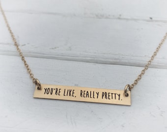 May include: A gold necklace with a bar pendant that reads "You're like, really pretty."