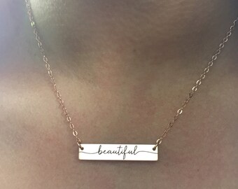 May include: A gold chain necklace with a bar pendant that says "beautiful" in cursive script.