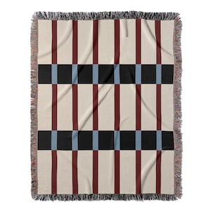 May include: A woven throw blanket with a geometric pattern. The design features alternating vertical stripes of burgundy and cream, intersected by black and light blue squares. The edges are finished with a fringe.