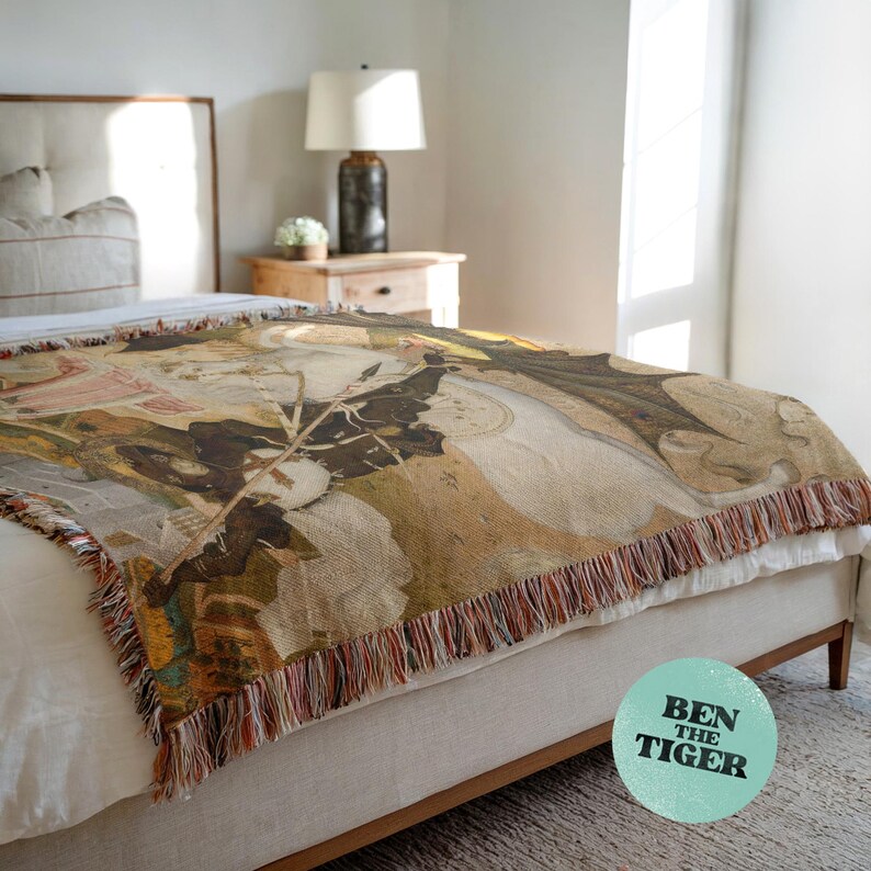 May include: A woven throw blanket with a detailed, vintage-style design in shades of brown, beige, and green, with a fringed edge. The blanket is draped over a bed. The text "BEN THE TIGER" is on a round sticker.