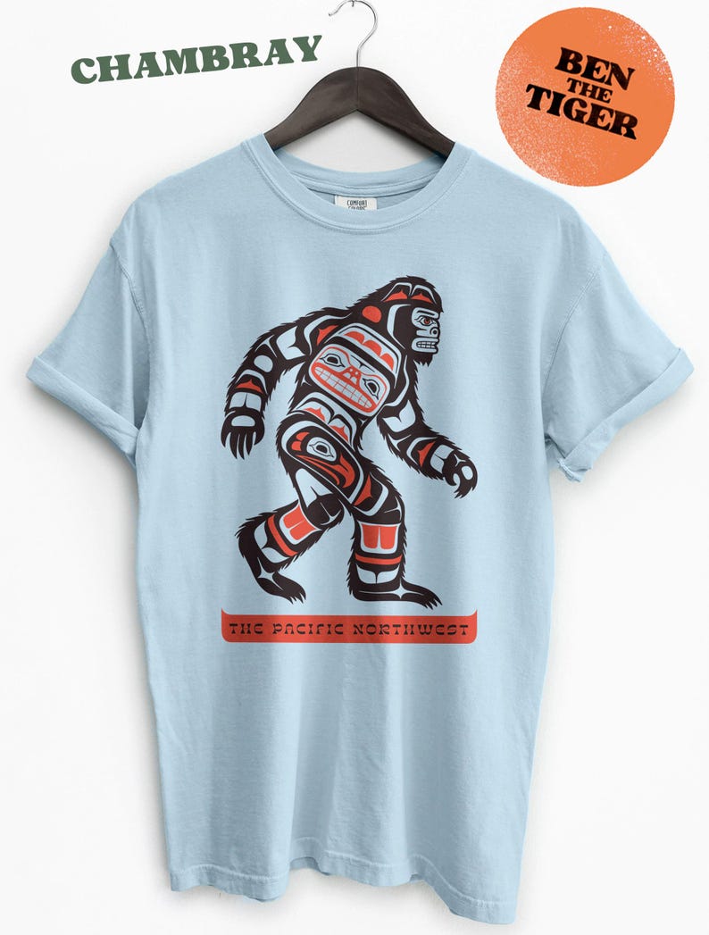 Puede incluir: Camiseta azul claro con un gr&aacute;fico de un Sasquatch estilizado en rojo, negro y blanco. El gr&aacute;fico est&aacute; rodeado del texto "The Pacific Northwest".