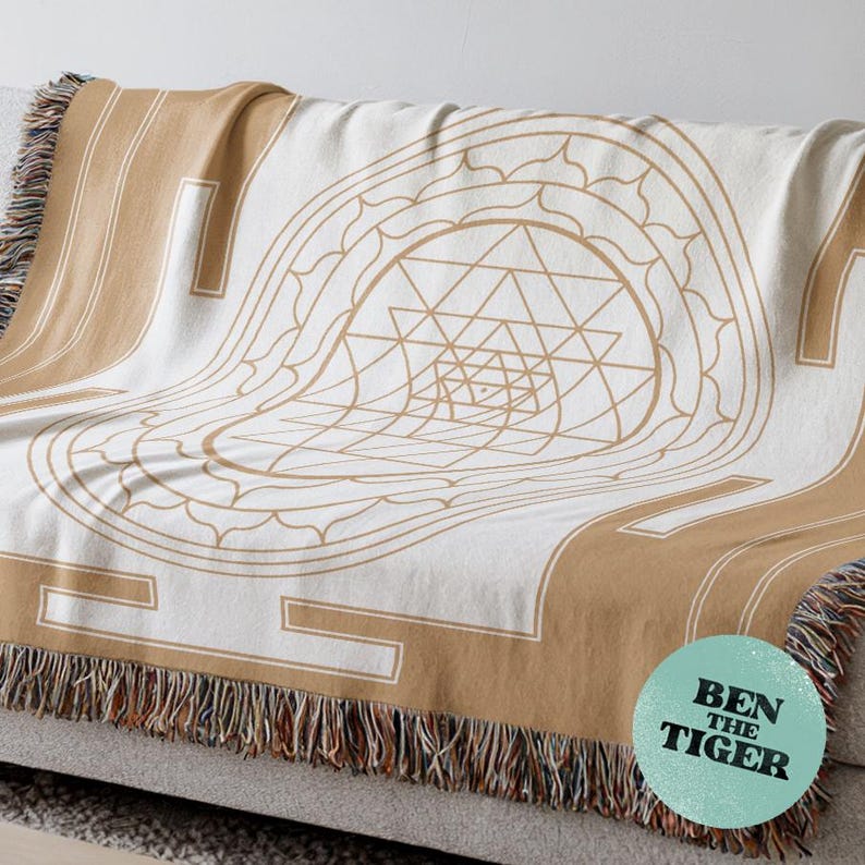 May include: A beige and white throw blanket with a geometric design and fringe. The blanket features a central geometric pattern in beige, framed by beige borders. The text "BEN THE TIGER" is on a teal circle in the lower right corner.