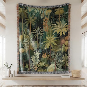 May include: A woven tapestry featuring a lush jungle scene with palm trees, ferns, and other tropical plants in shades of green, brown, and yellow. The tapestry has a black background and fringed edges.