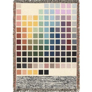 Pode incluir: Cobertor tecido com um padrão de quadrados coloridos em tons de rosa, amarelo, verde, azul e roxo. O cobertor tem um fundo creme e uma borda com franjas. A parte inferior apresenta uma faixa texturizada em preto e branco.