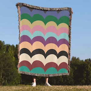 Op de afbeelding: Een rechthoekige geweven plaid met een herhalend patroon van horizontale geschulpte bogen in diverse kleuren, waaronder groen, geel, roze, lichtblauw, paars, perzik, zwart, crème, bordeauxrood en talingblauw, afgewerkt met een franjerand.