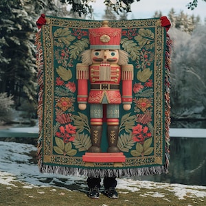 May include: A large, decorative tapestry featuring a detailed illustration of a nutcracker soldier in red, gold, and blue. The tapestry has a green background with floral and leaf patterns, and a fringed edge. The nutcracker is standing on a red base.