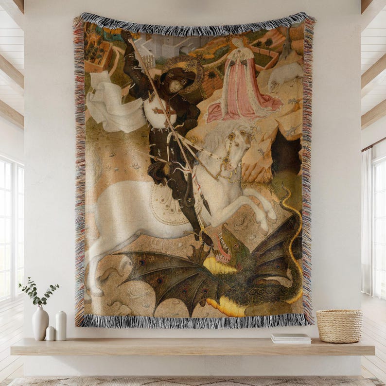 May include: Woven tapestry throw blanket featuring a medieval painting of a knight on horseback slaying a dragon. The artwork depicts a knight in black armor, a white horse, and a green dragon. The blanket has a fringed edge.