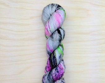 May include: A skein of yarn with a speckled pattern in shades of gray, pink, and green.