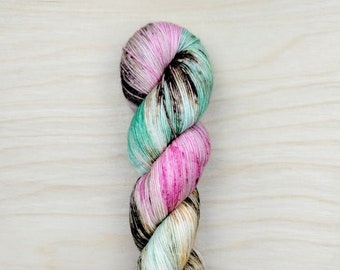 May include: A twisted skein of yarn in a variety of colors. The yarn features pink, green, black, and tan hues. The yarn is tightly wound and appears soft, suitable for knitting or crocheting projects.