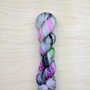 May include: A skein of yarn with a speckled pattern in shades of grey, pink, and green.
