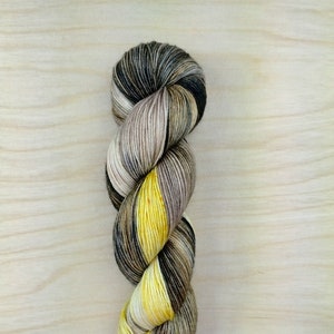 Könnte beinhalten: Eine Garnrolle mit einem melierten Farbmuster in Schwarz, Braun, Beige und Gelb.