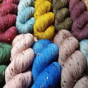May include: A collection of colorful yarn skeins with flecks of black throughout. The yarn is arranged in a circle with the ends of the skeins overlapping.