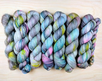 May include: Eight skeins of yarn in various shades of blue, green, gray, and pink. The yarn is arranged in a row, with the ends of the skeins overlapping.