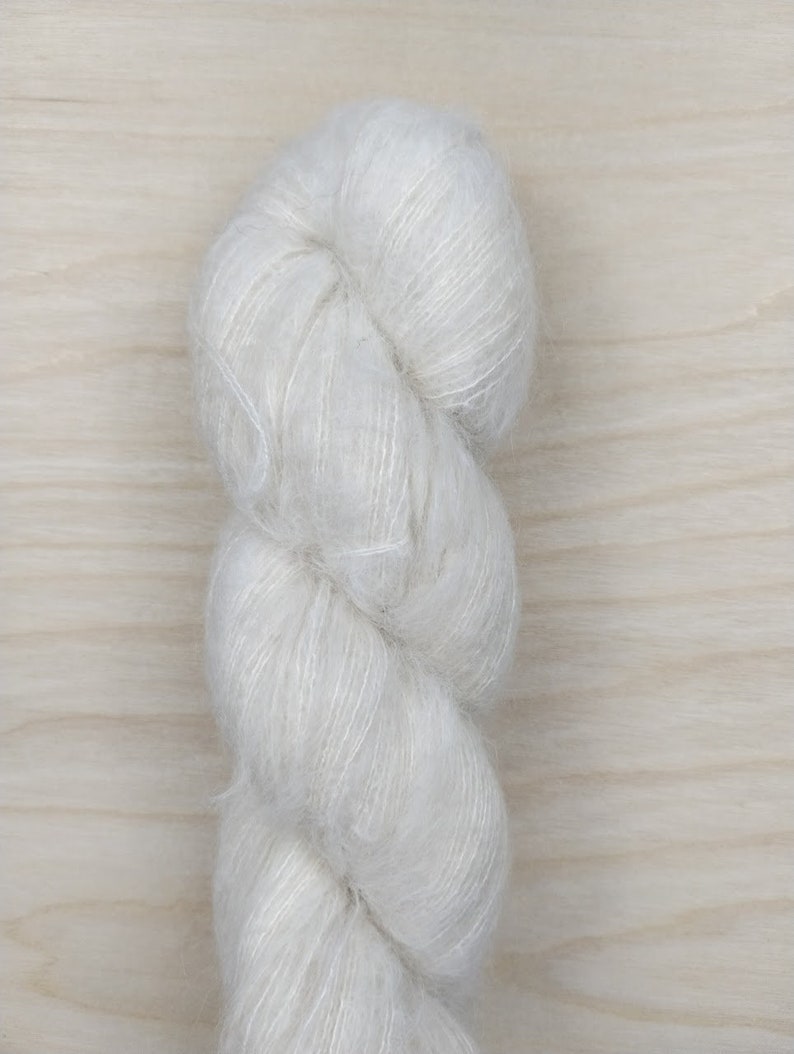 May include: A skein of white yarn with a soft, fluffy texture.