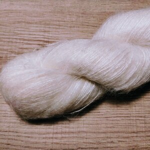 May include: A skein of soft, white yarn with a delicate, fuzzy texture. The yarn is loosely wound and appears to be made of a blend of fibers.