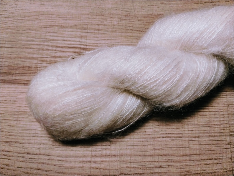 May include: A skein of soft, white yarn with a delicate, fuzzy texture. The yarn is loosely wound and appears to be made of a blend of fibers.