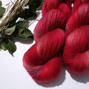 May include: Two skeins of red yarn with subtle pink and orange highlights. The yarn is soft and fluffy, perfect for knitting or crocheting.