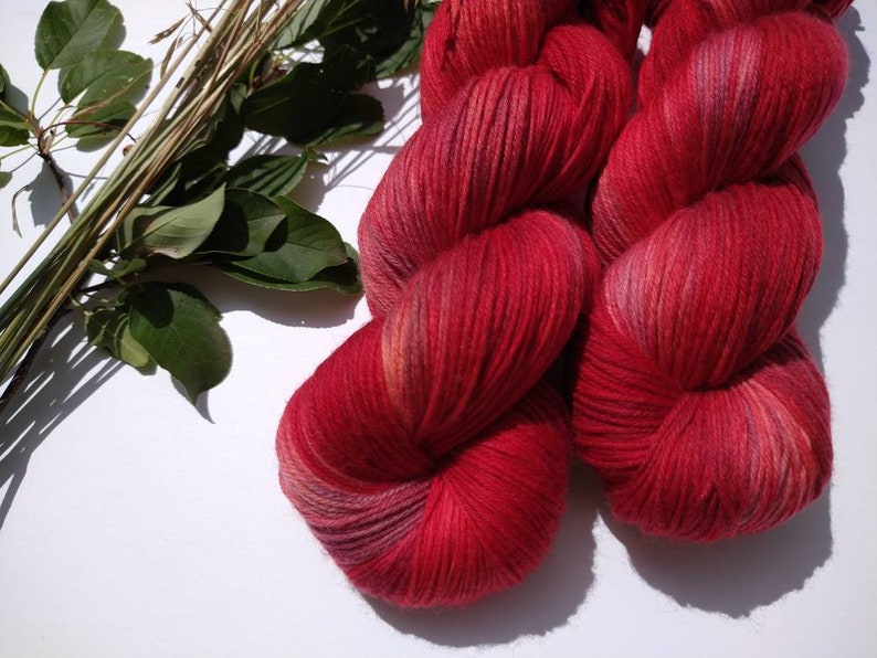 May include: Two skeins of red yarn with subtle pink and orange highlights. The yarn is soft and fluffy, perfect for knitting or crocheting.